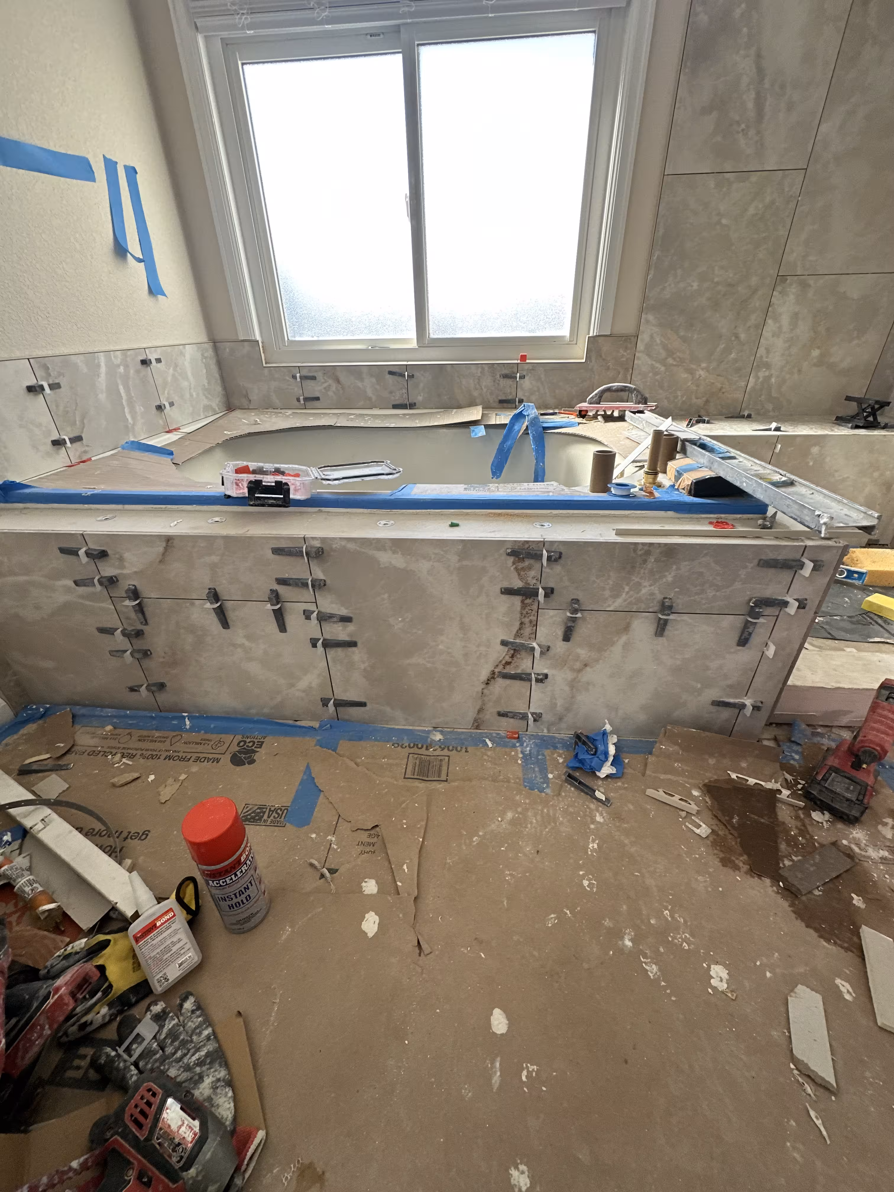 Tub deck and apron tile installation in progress with leveling clips across multiple courses beneath the window, Highlands Ranch master bath