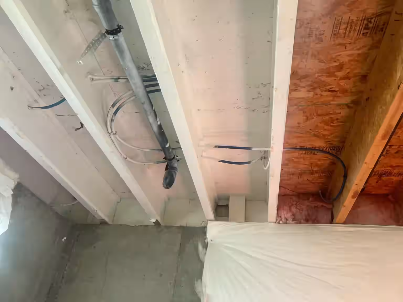 Ceiling joist and plumbing installation viewed from room below second-floor shower