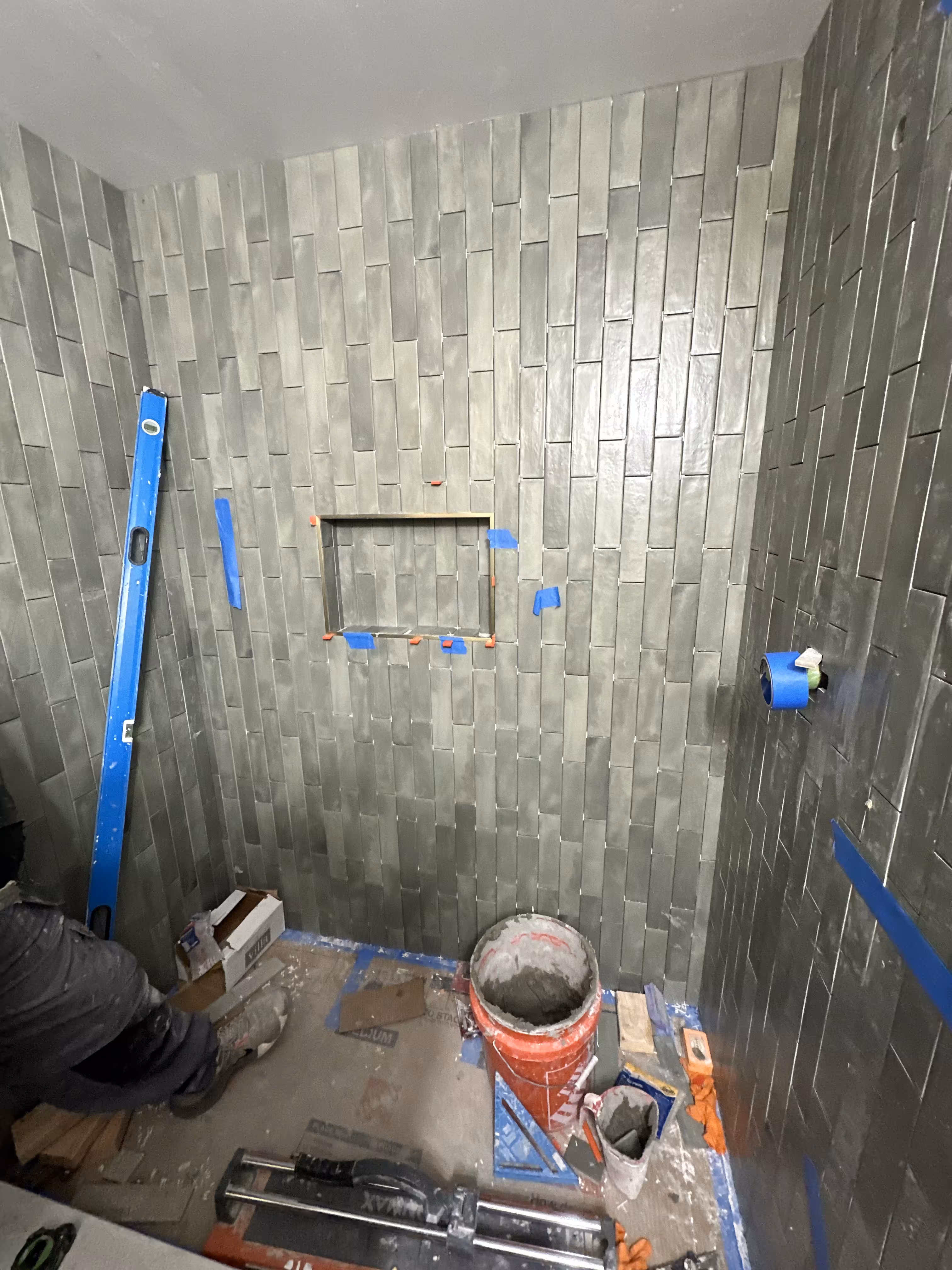 Green stacked tile shower walls with a metal-trimmed niche taped off before grouting