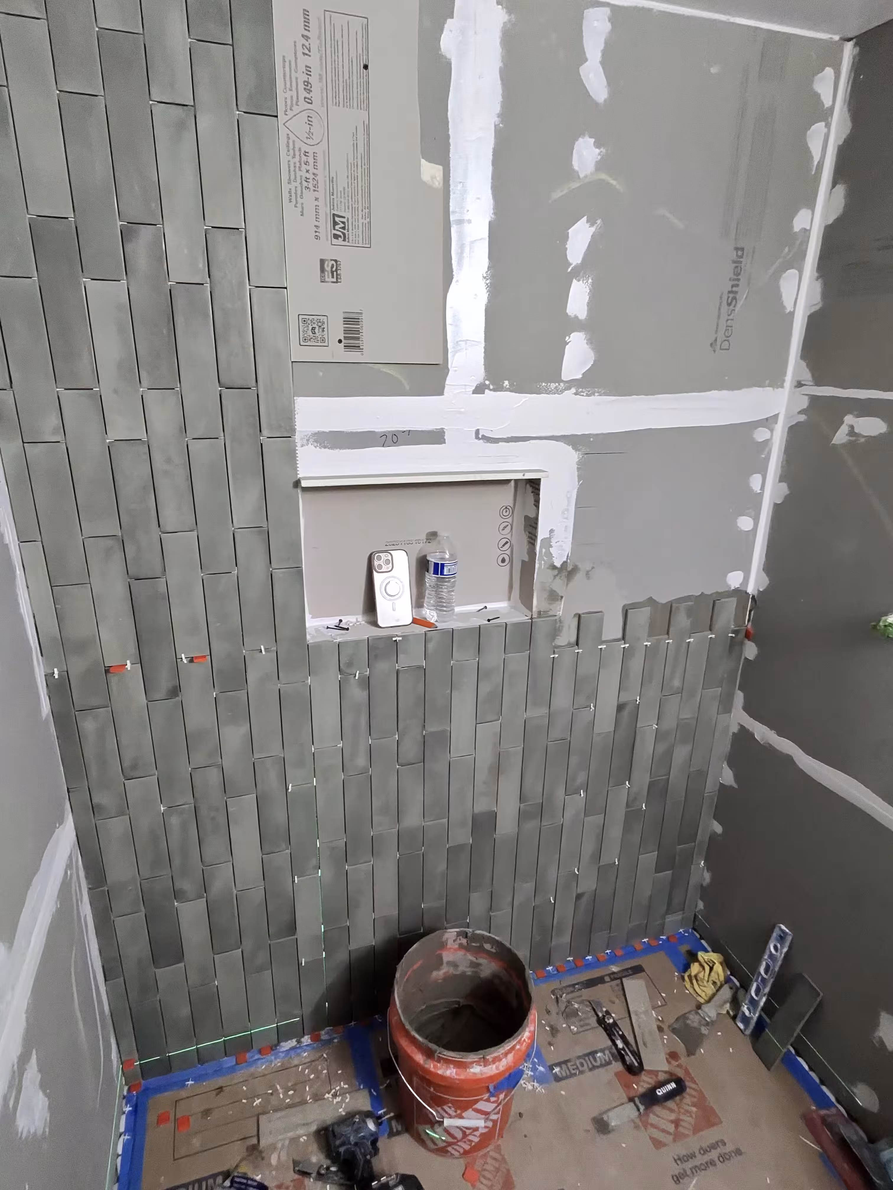 Green vertical stacked tile being installed partway up the shower wall in Commerce City