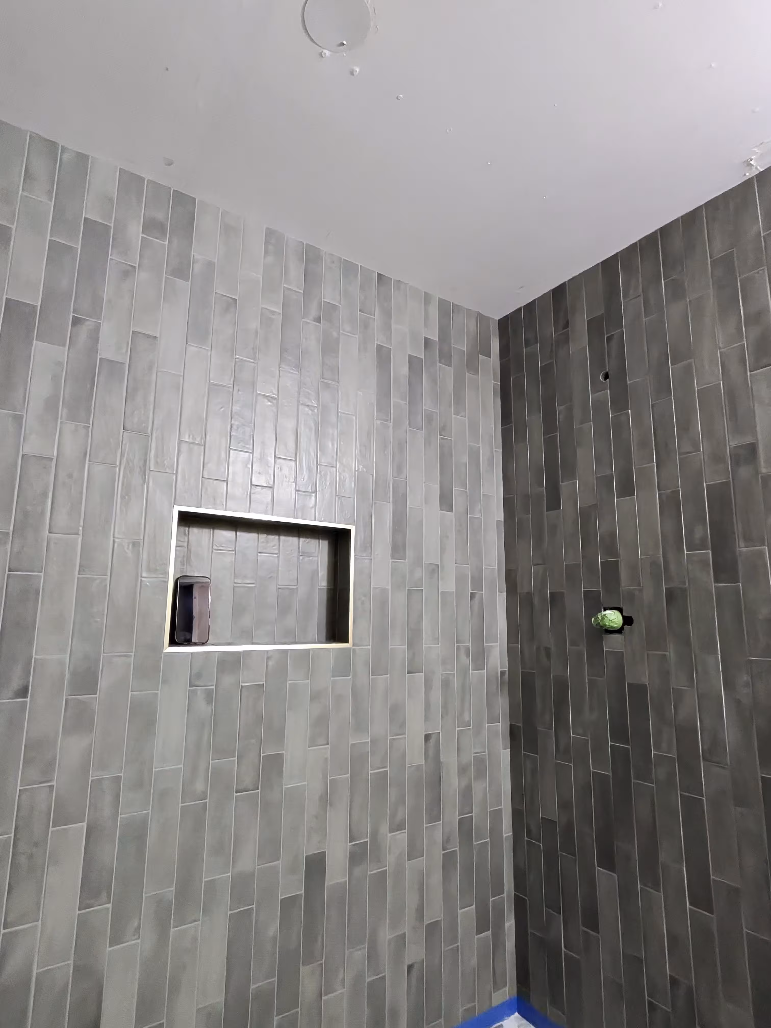 Finished green stacked tile shower walls meeting at the corner with the niche complete