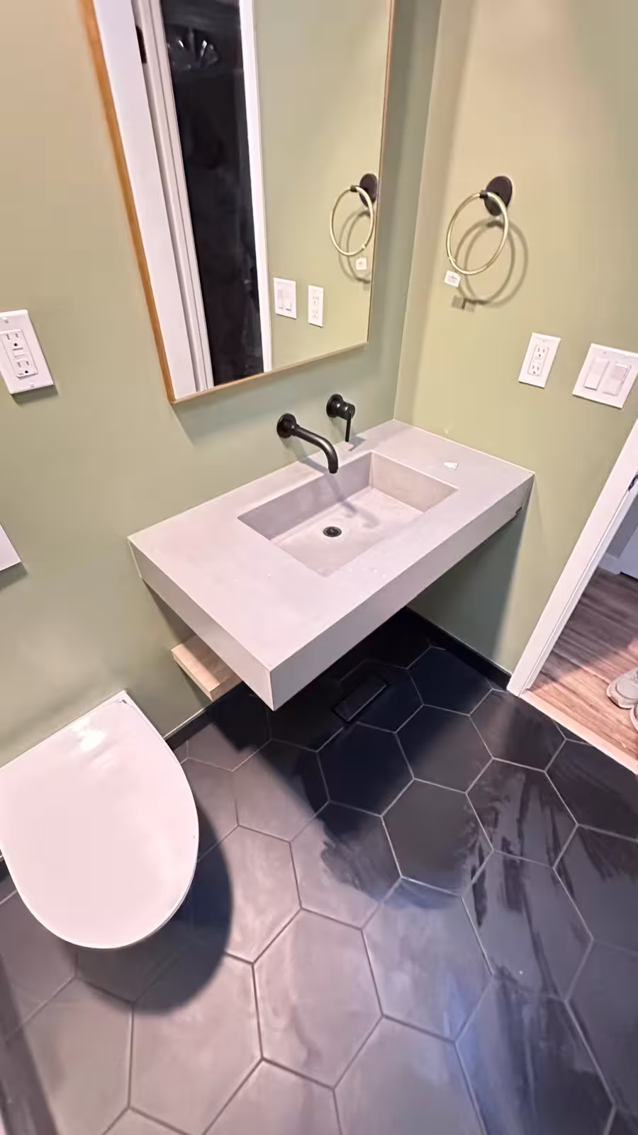 Custom concrete sink with wall-mounted faucet and black hexagon floor tile in designer bathroom