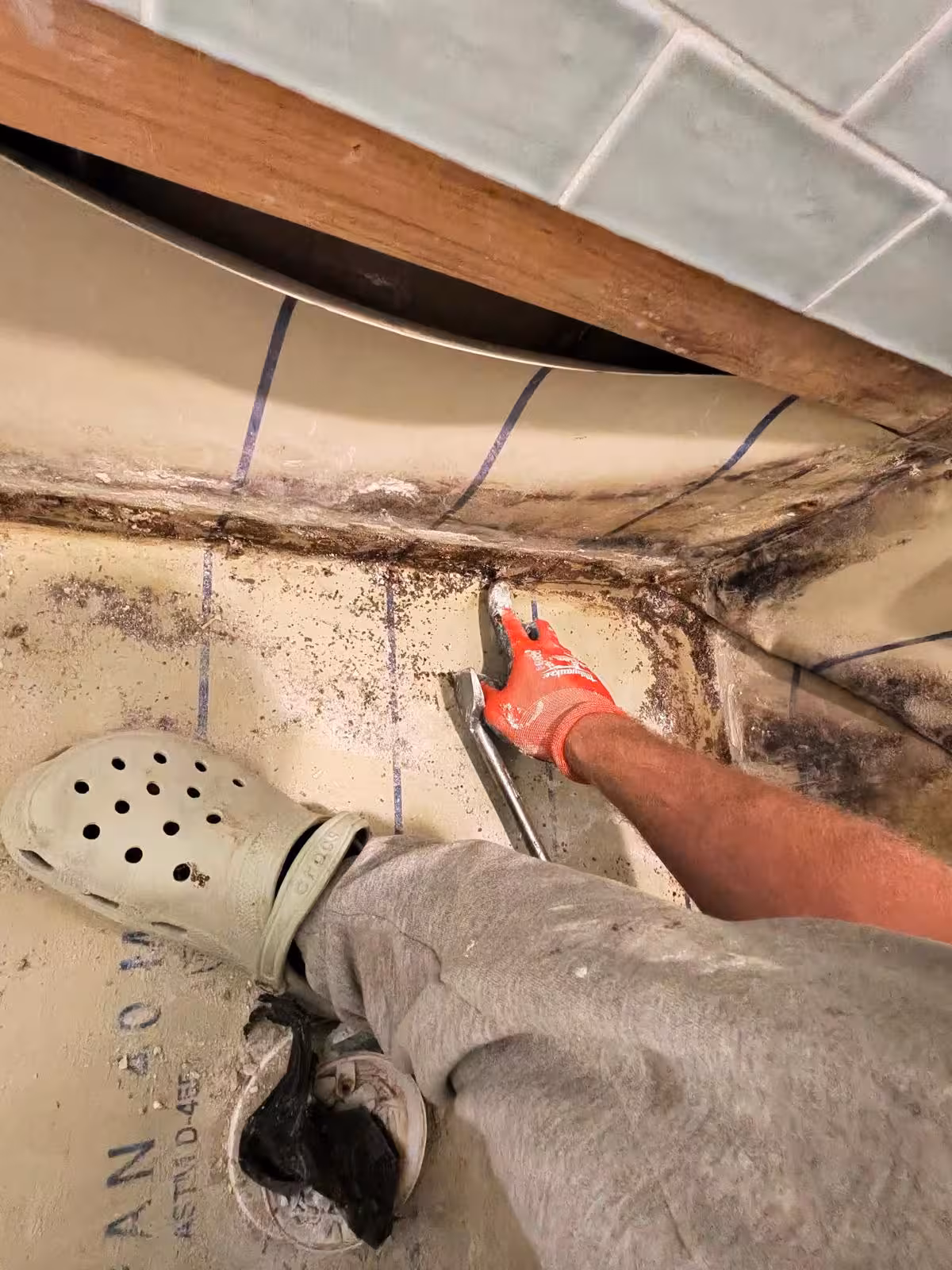 Scraping old mortar from shower pan during repair process Denver