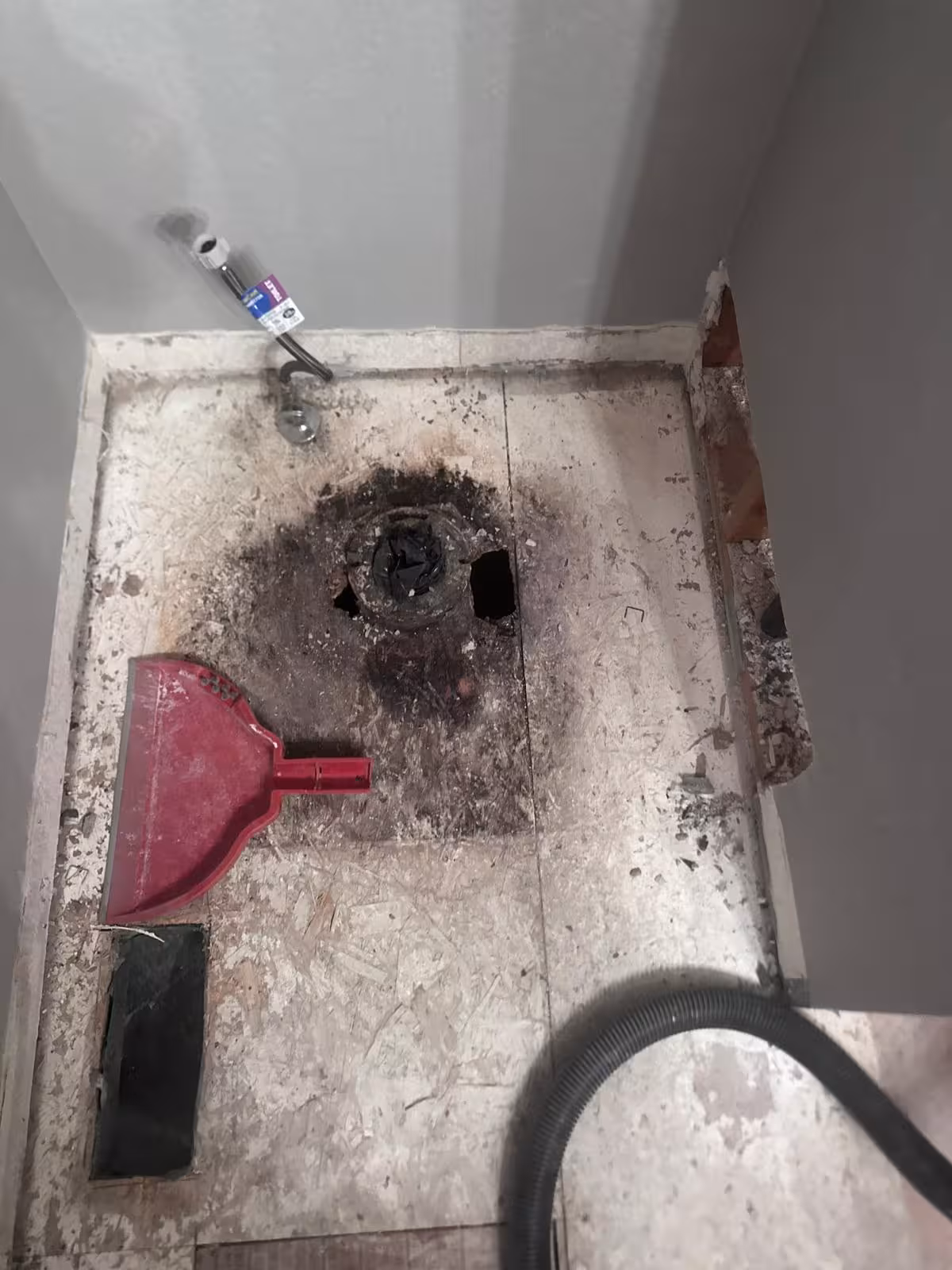 Old shower demolition revealing damaged plywood and drain assembly