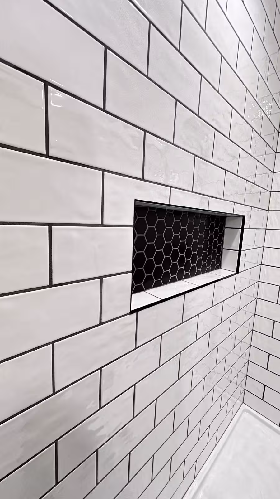 Custom shower niche with black hexagon tile accent in white subway tile
